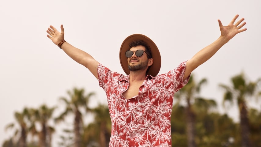 Designs That Work Well With Sublimation Printing A man wearing a sublimated Hawaiian shirt with a pattern of red and white palm trees.