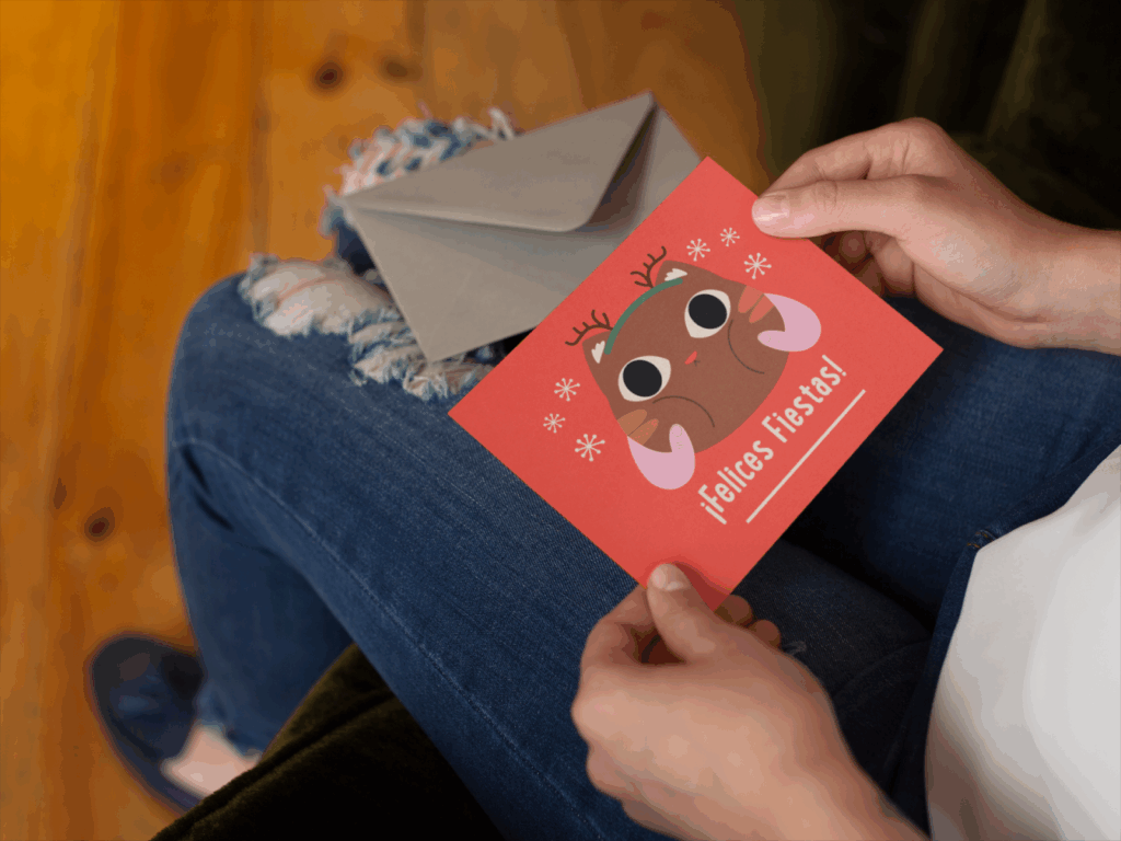 06 Inclusive and multilingual holiday greetings A woman smiles while holding a Christmas card featuring a moose design.