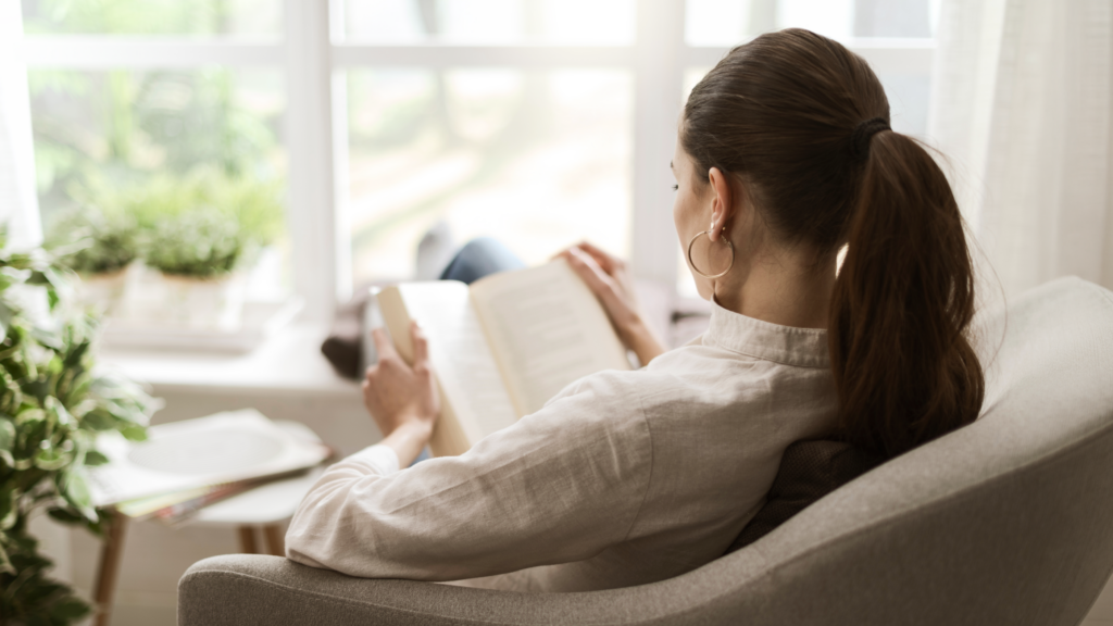 13 Best affiliate marketing books A woman sits in a chair, engrossed in reading a book, surrounded by a cozy atmosphere.