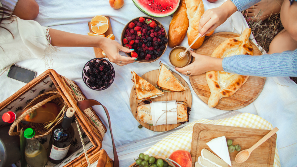 3 9 Barbecue party essentials for summer gatherings A vibrant picnic scene on a white blanket features sliced watermelon, berries, pastries, and a cheese platter.