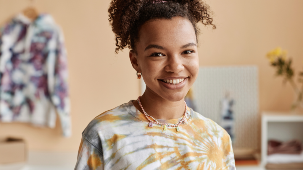 4 Unique tie dye patterns that stand out on product pages Smiling person in a tie-dye shirt and necklace stands in a cozy room.