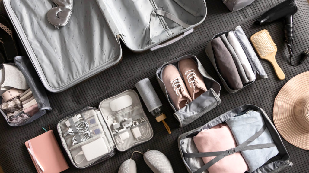 6 4 Best travel accessories for summer sales Open suitcase with neatly arranged items around: shoes, clothes, toiletries, tech gadgets, hairbrush, and a hat.