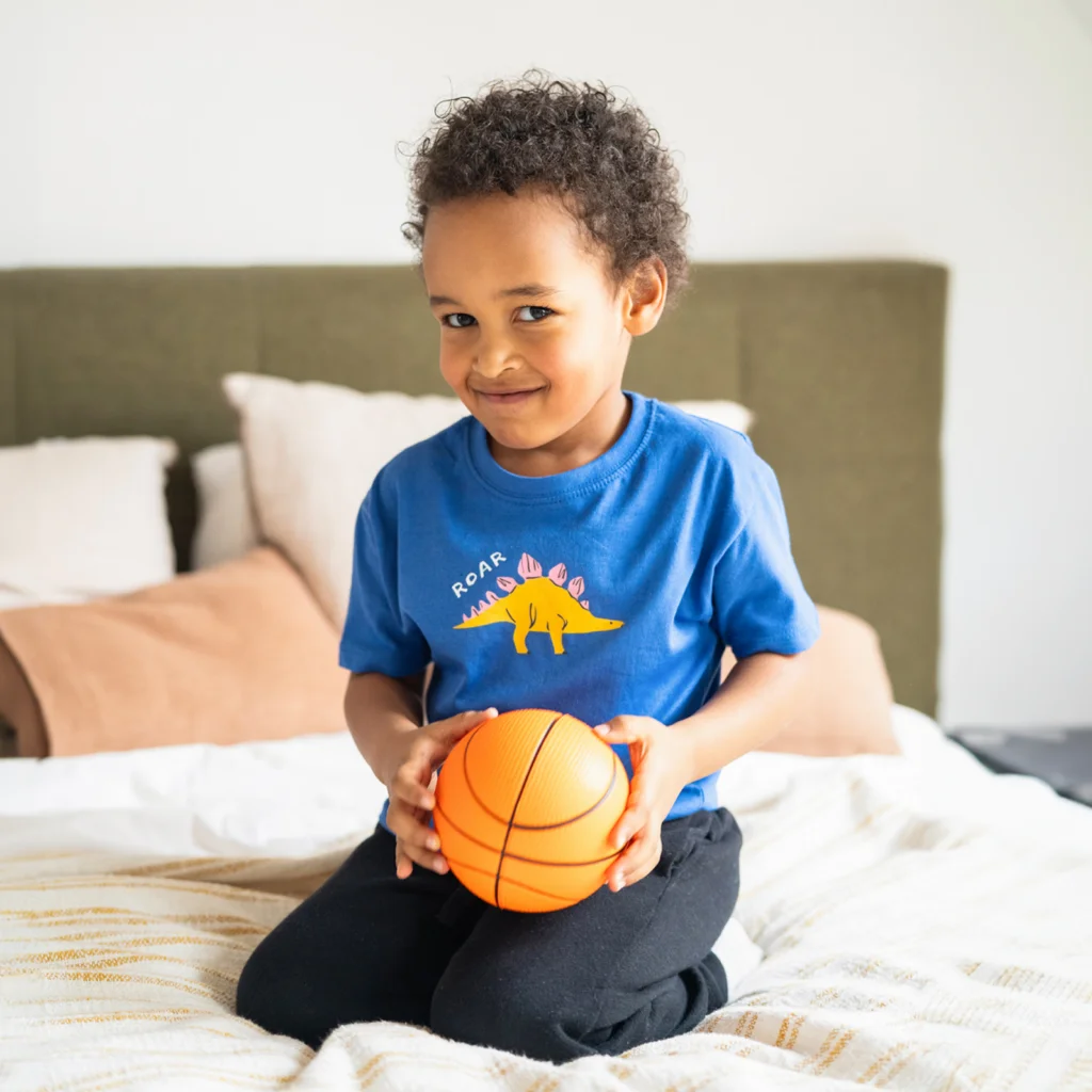 A young boy playing with a basketball wearing a custom blue “Roar” t-shirt with a dinosaur print.