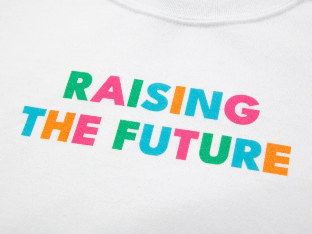 Best print on demand products to sell on Etsy Bold, multi-colored text reading "Raising the Future" is printed on a white t-shirt.