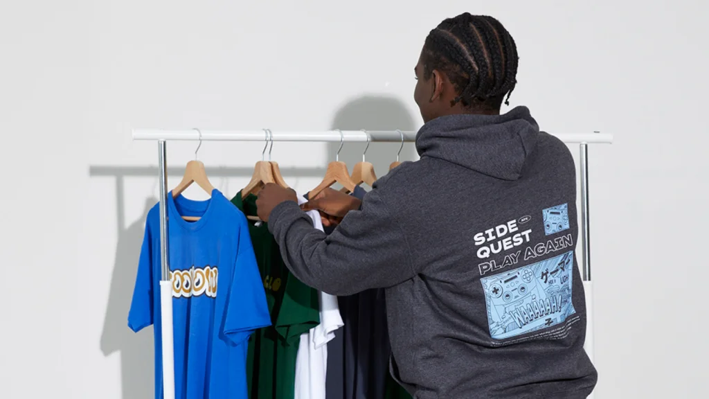 Choose shirts and design them A man in a graphic hoodie looks at colorful t-shirts on a clothing rack.