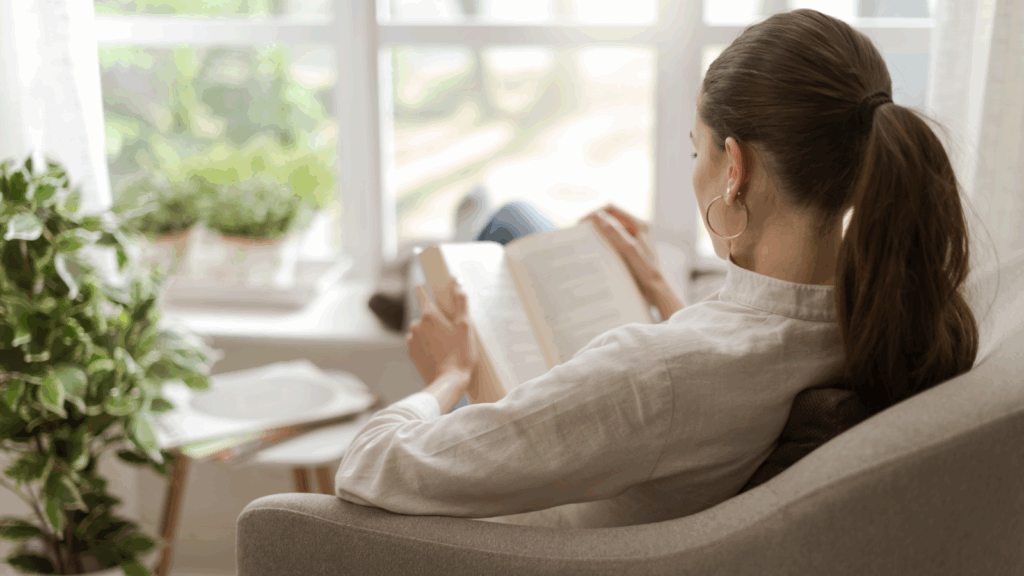 Literary girl A woman sits in a chair, engrossed in reading a book, surrounded by a cozy atmosphere.