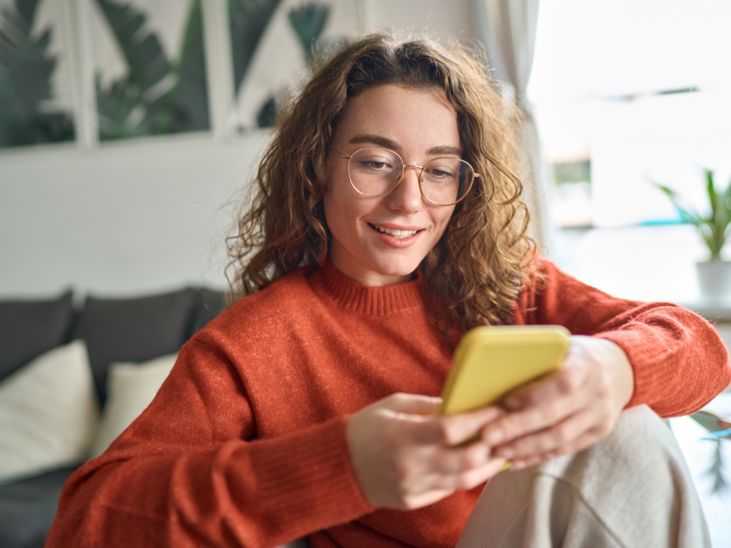 A woman in glasses is focused on her phone, exploring a mobile-friendly site with interest.