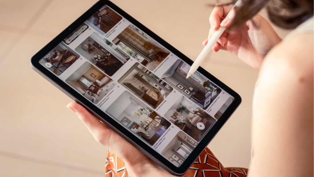 A woman holds a tablet displaying a photo of a house, smiling as she looks at the screen.